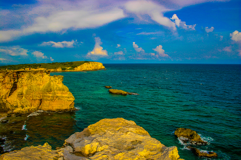 Caribbean coastline panorama — turquoise water meets rugged cliffs and a distant headland
